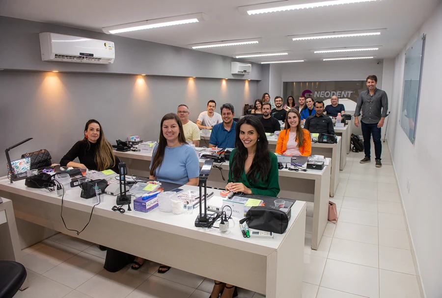 Grupo de alunos concentrados em atividades práticas em sala de aula, com materiais odontológicos e equipamentos sobre as mesas.