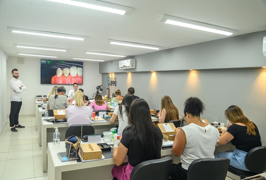 Vista de uma sala de aula do Instituto IPPO, com alunos em suas mesas prestando atenção a uma aula prática de odontologia.