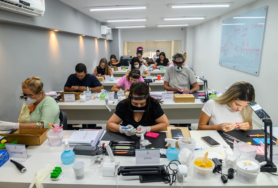 Instrutor do Instituto IPPO observando alunos que realizam práticas odontológicas em modelos, em uma sala iluminada e moderna.