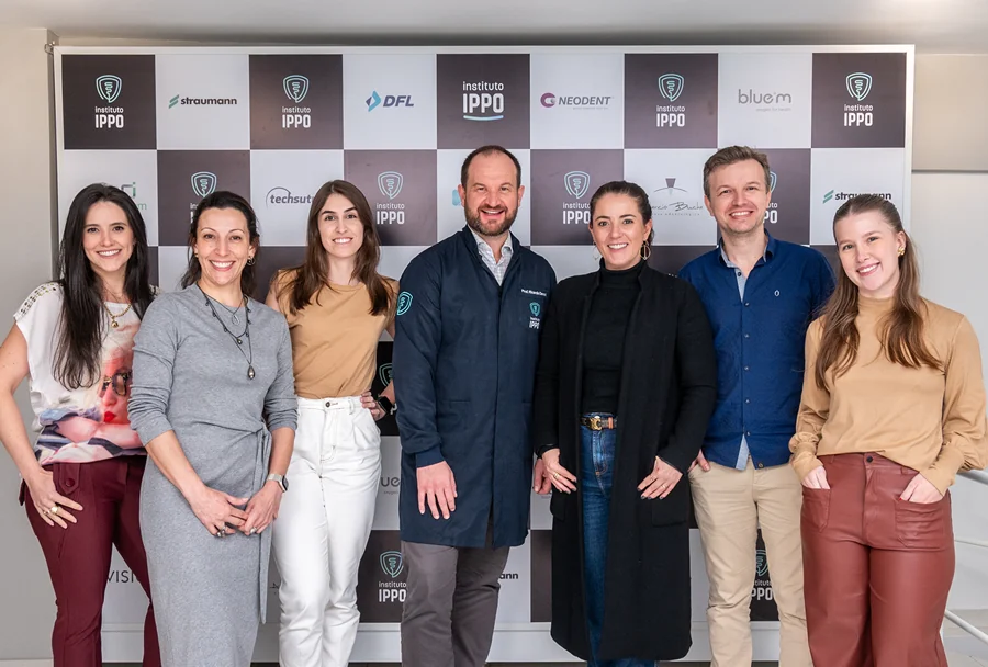 Grupo de profissionais posando para uma foto em frente a um banner do Instituto IPPO, com logomarcas de patrocinadores ao fundo.