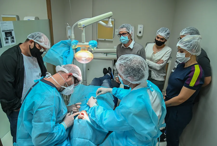 Visão lateral de uma cirurgia guiada, com os alunos assistindo enquanto o professor e assistentes realizam o procedimento.